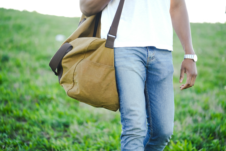 man carrying duffle bag on a grassy hill