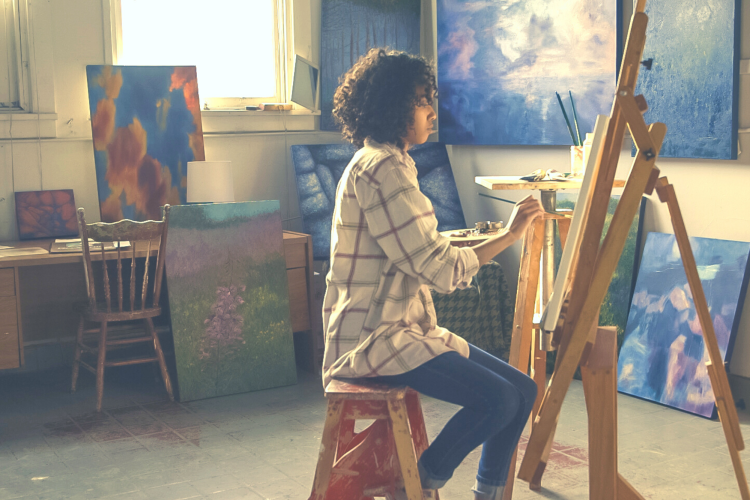 woman painting on canvas in dim room