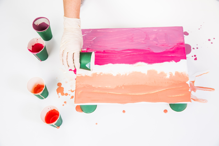 pouring pink and orange paint onto blank canvas