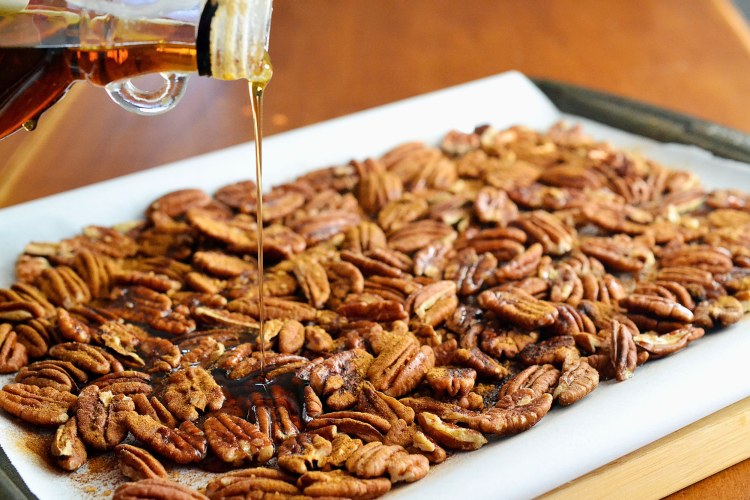 pouring maple syrup on baking sheet of pecans