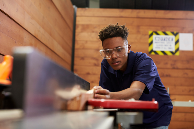 teen boy sawing in woodshop class