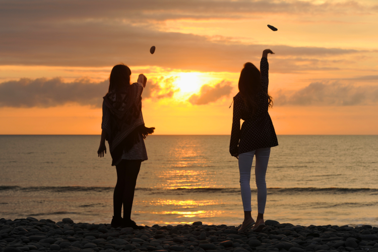 women throwing stones into body of water