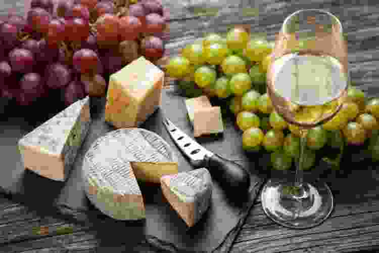 cheese on a slate board with grapes and white wine