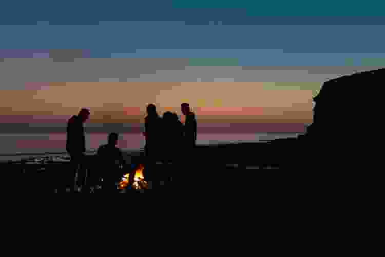 friends gathered around a beach bonfire at sunset