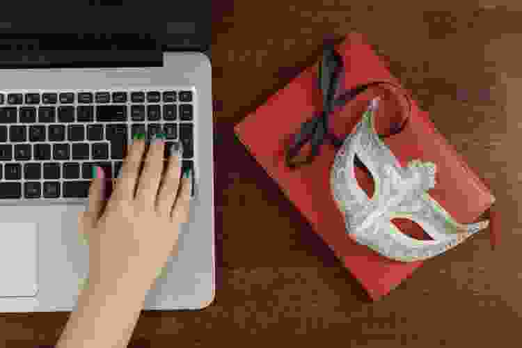 hand on laptop next to masquerade mask