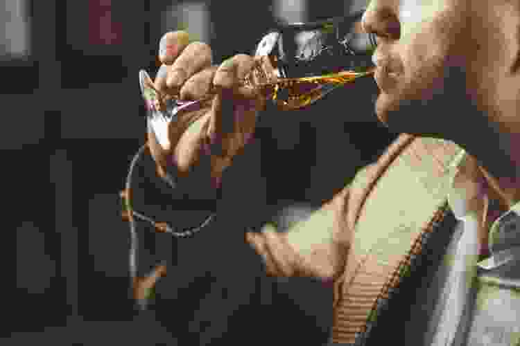 person taking sip of whiskey from glass