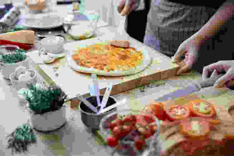 hands spreading sauce on pizza dough