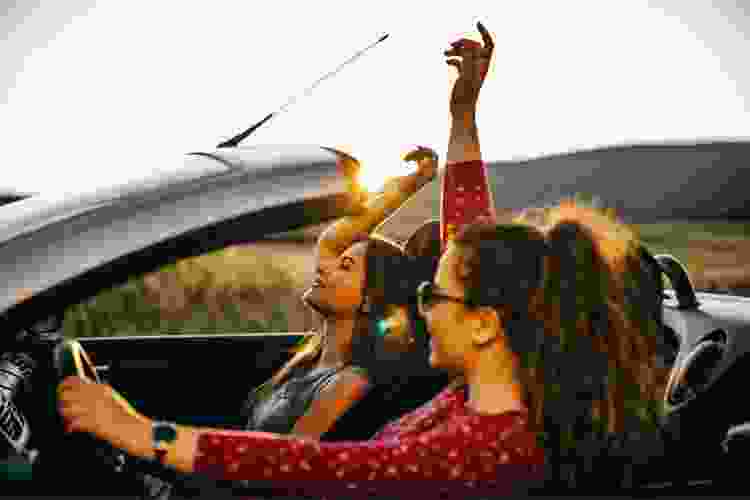 two women in convertible car with hands up