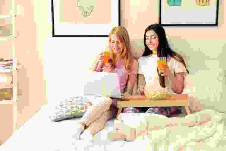 two people in pajamas in bed with laptop. popcorn and drinks