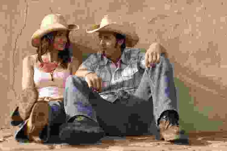 two people sitting dressed in cowboy hats, jeans and boots