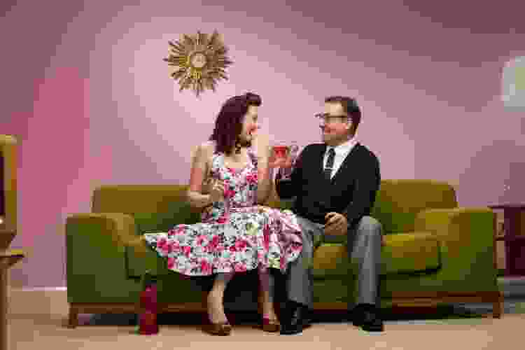 two people dressed in 1950s clothes drinking cocktails on a couch