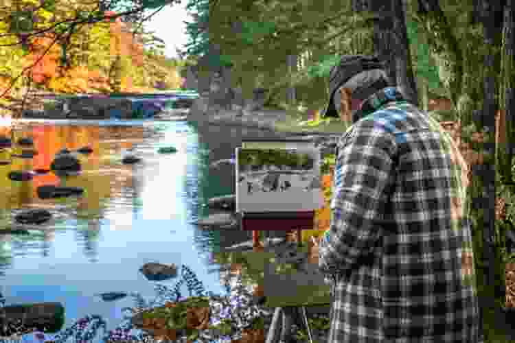 man painting canvas on easel by fall stream