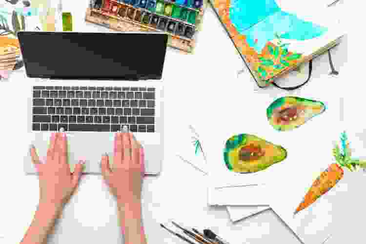 hands on laptop surrounded by watercolor paintings