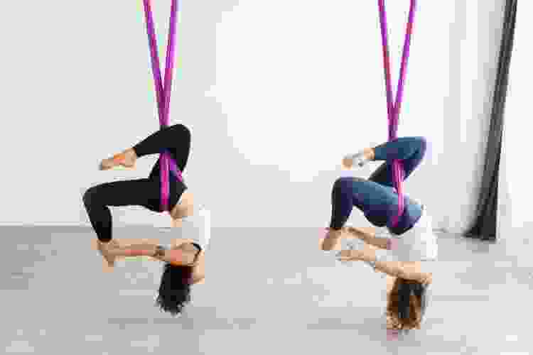 two woman upside down in aerial yoga class