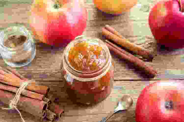 jar of apple butter next to apples and cinnamon sticks