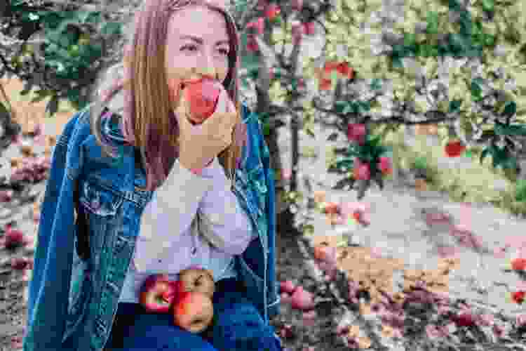 young woman biting into apple in apple orchard