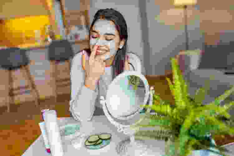 woman doing a mud mask at her vanity mirror