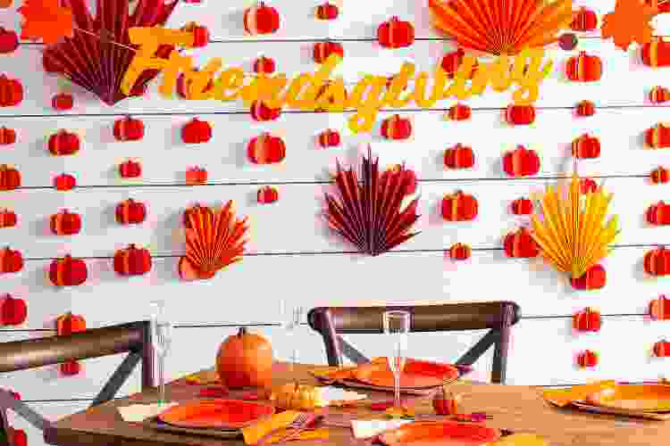 Friendsgiving banner and fall leaf paper décor behind dining table