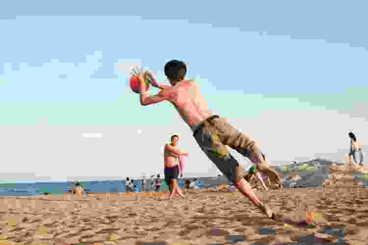 teens playing catch with ball on the beach