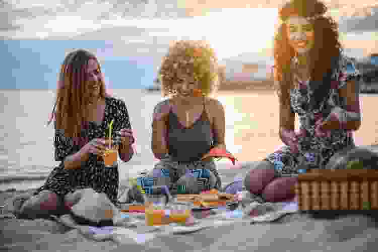 group of friends having picnic on the beach