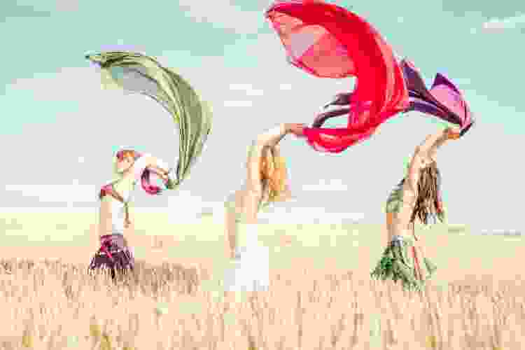 three women with scarves belly dancing in a field