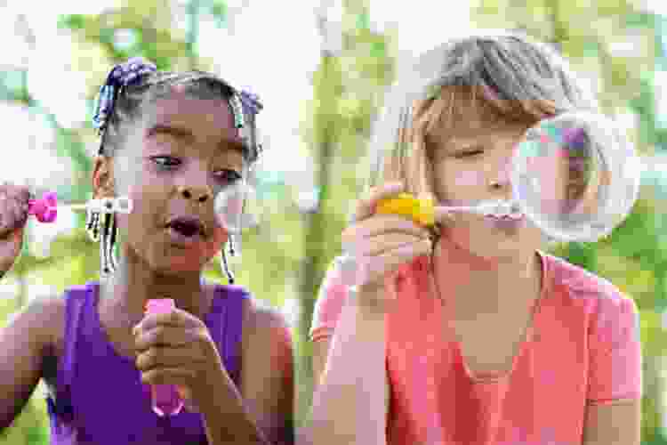 two young children blowing bubbles outside