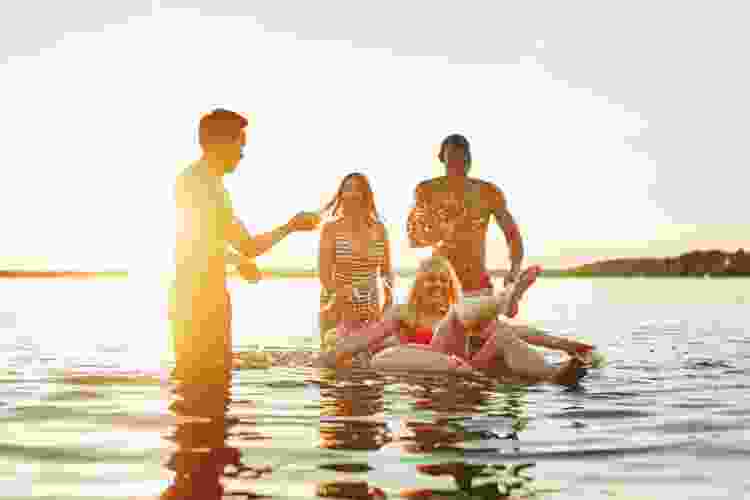 college friends swimming in lake at sunset