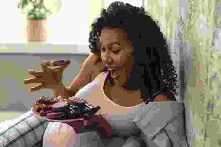 pregnant woman smiling at a plate of cookies and chocolates