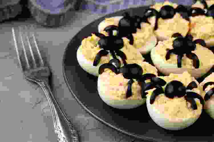 plate of deviled eggs with olives shaped like spiders