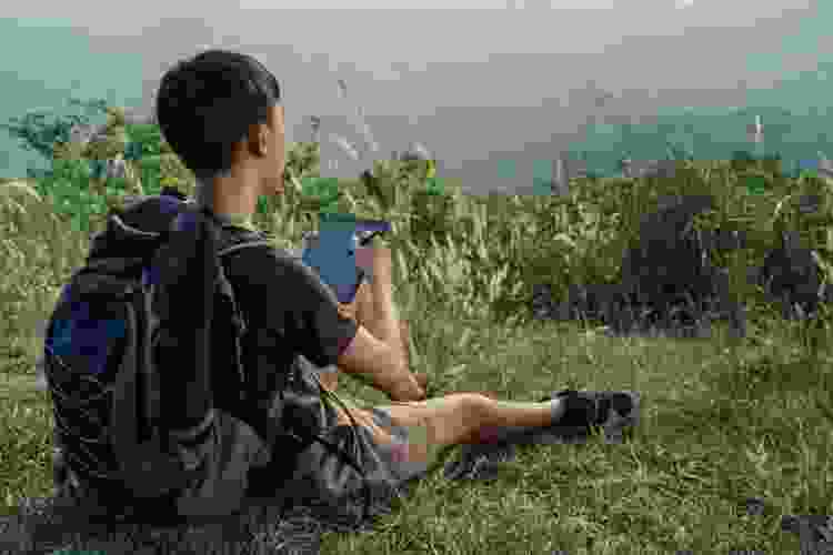 young man overlooking scenic cliff while writing on digital tablet