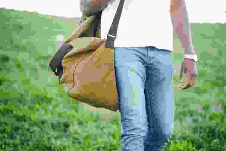 man carrying duffle bag on a grassy hill