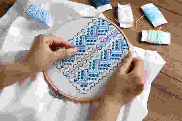 hands threading blue thread through needlepoint ring