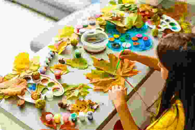 young hands making fall crafts with leaves and paint