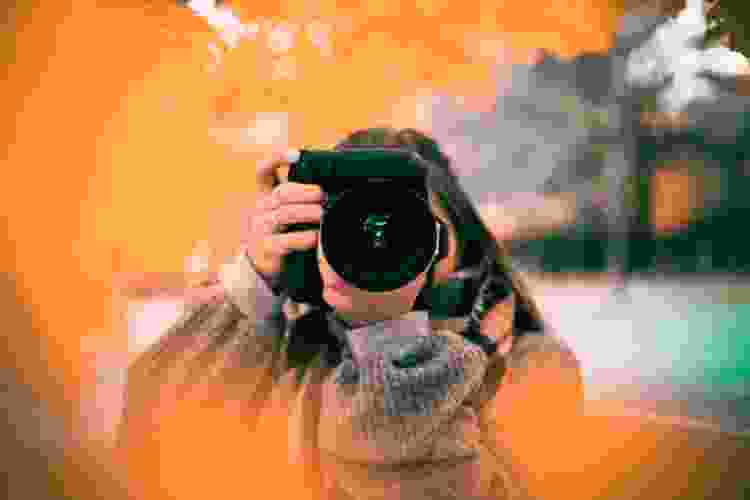 woman holding camera with orange fall leaves in the foreground