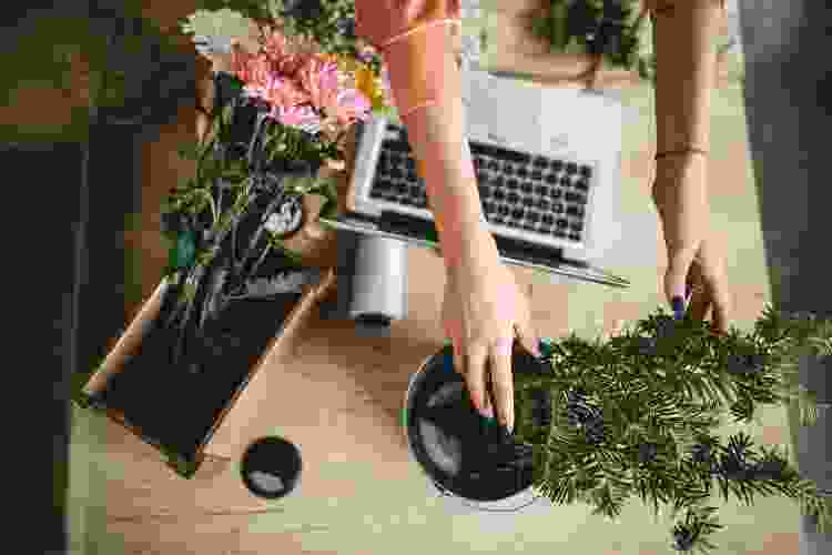 hands arranging flowers near laptop