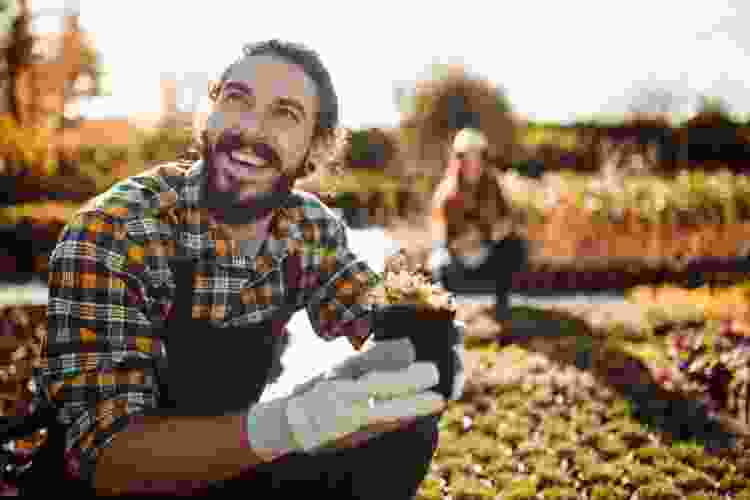 man smiling as he plants seeds in his garden