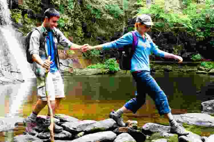 couple hiking across rocks in creek 