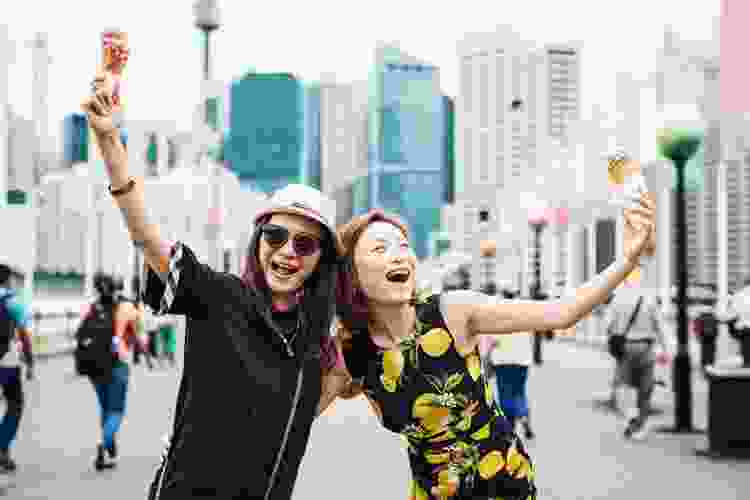 two smiling friends in street eating fresh ice cream