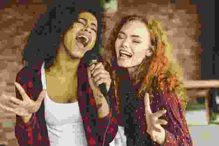 two young women singing karaoke together at home