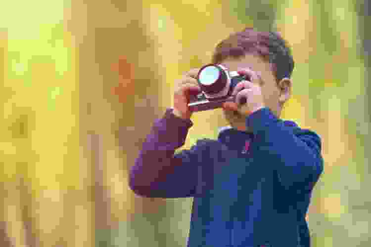 young boy taking photos with camera at sunset