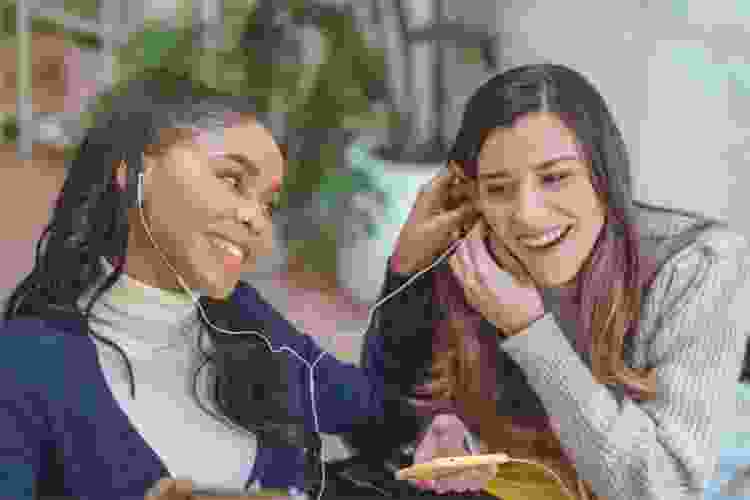 two young women sharing headphones listening to music