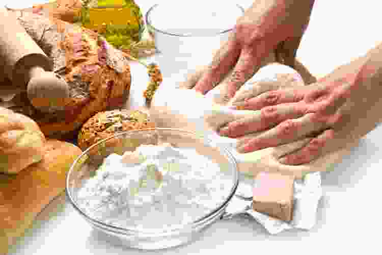 hand kneading dough next to baked bread and olive oil