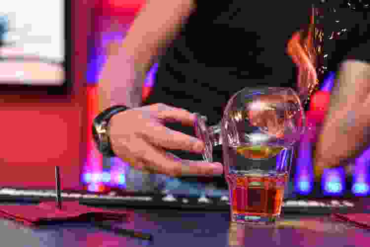 hand pouring cup of flame into cocktail