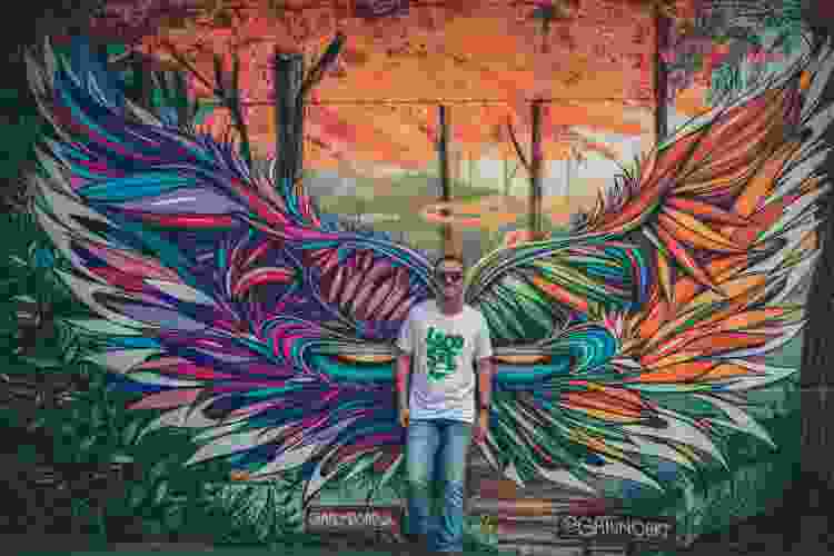 man standing in front of colorful wings mural