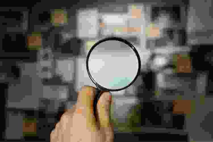 hand holding magnifying glass up to photos and clues