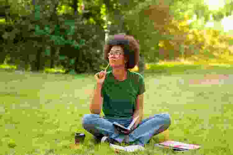 woman journaling surrounded by green grass and trees