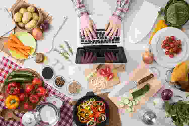 hands on laptop surrounded by ingredients and cooking supplies