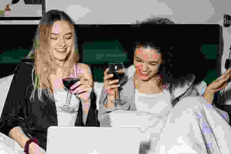 two friends drinking wine and playing games online with laptop