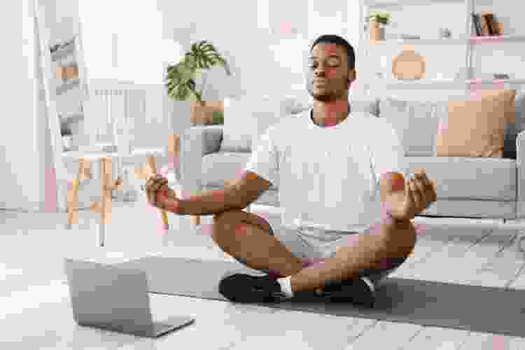 young man doing yoga at home with laptop