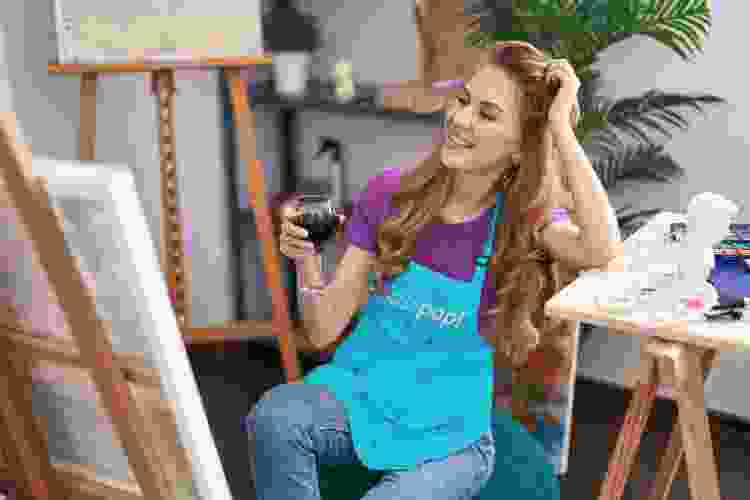 young woman painting canvas while sipping red wine